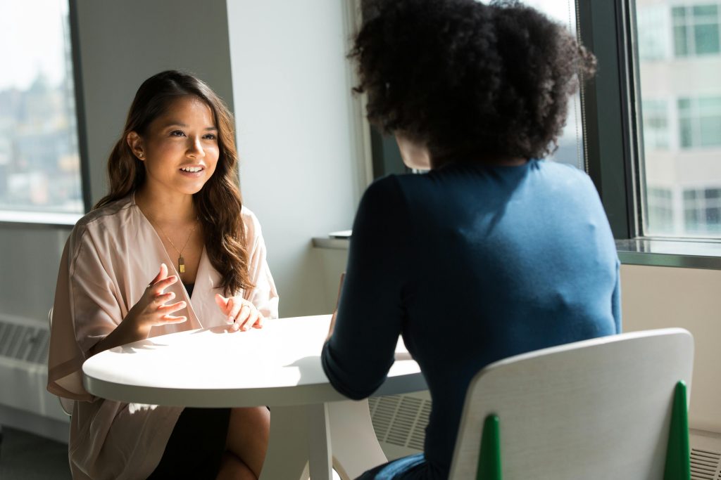 pexels-photo-1181715-1181715 Two women sitting at a table having a professional discussion in a bright office setting.